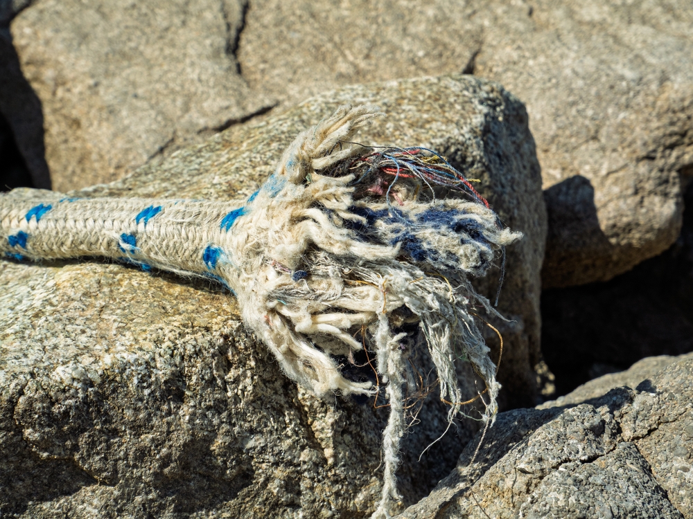 Close-up of a frayed end of a boating rope sitting on a rock
