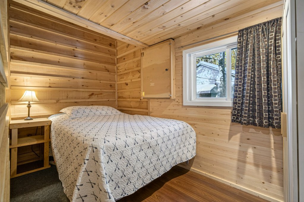 Bedroom with wood-paneled walls, double bed, bedside table, and window.