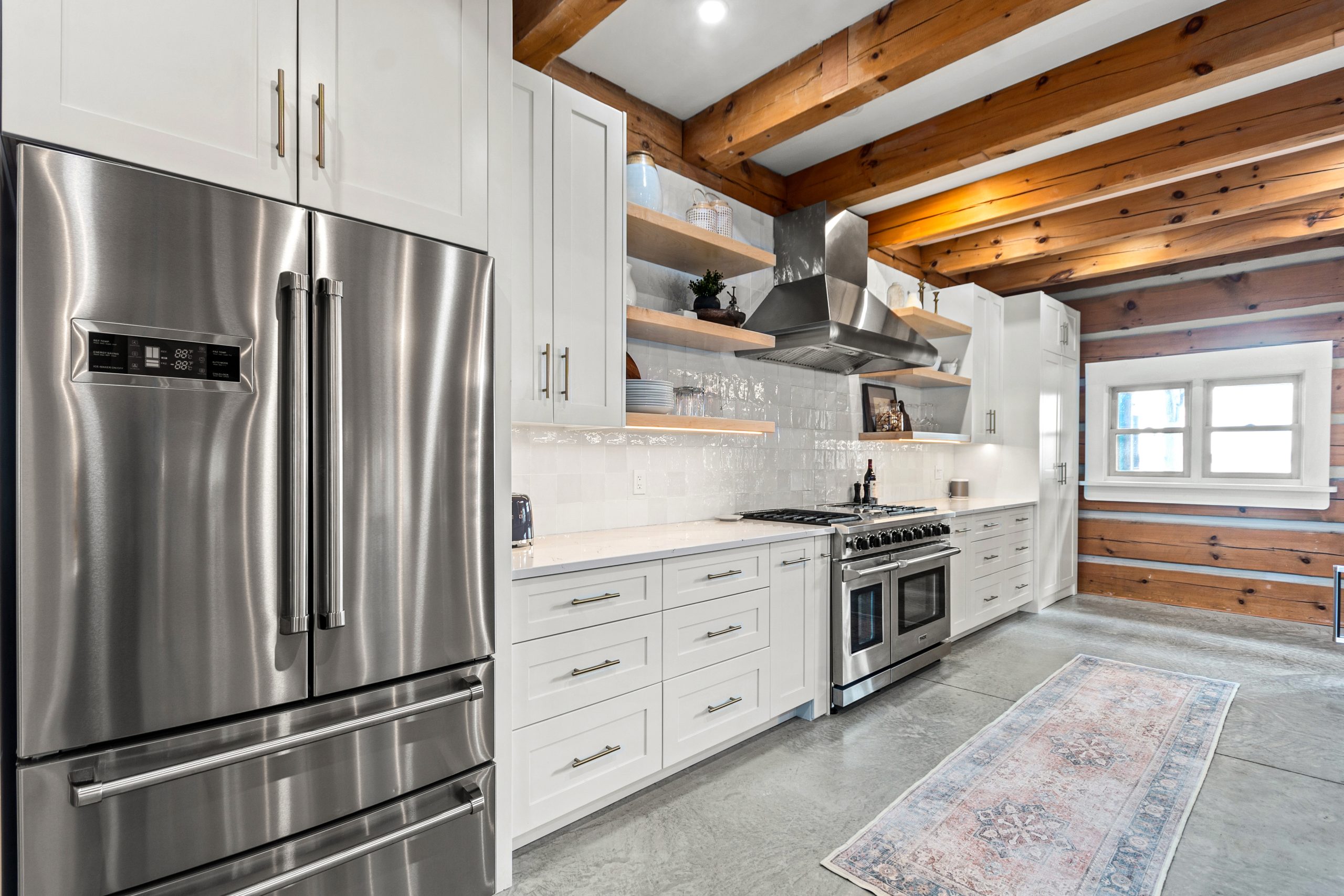 Kitchen view with stainless-steel refrigerator, white cabinetry, open shelving, and exposed wood beams overhead.