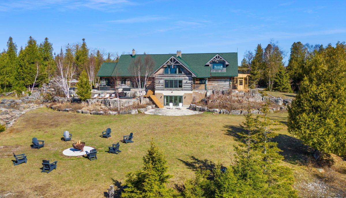 Aerial view of the main lodge and lawn at 221 Pennie Avenue, with outdoor seating and forest surrounding the property.