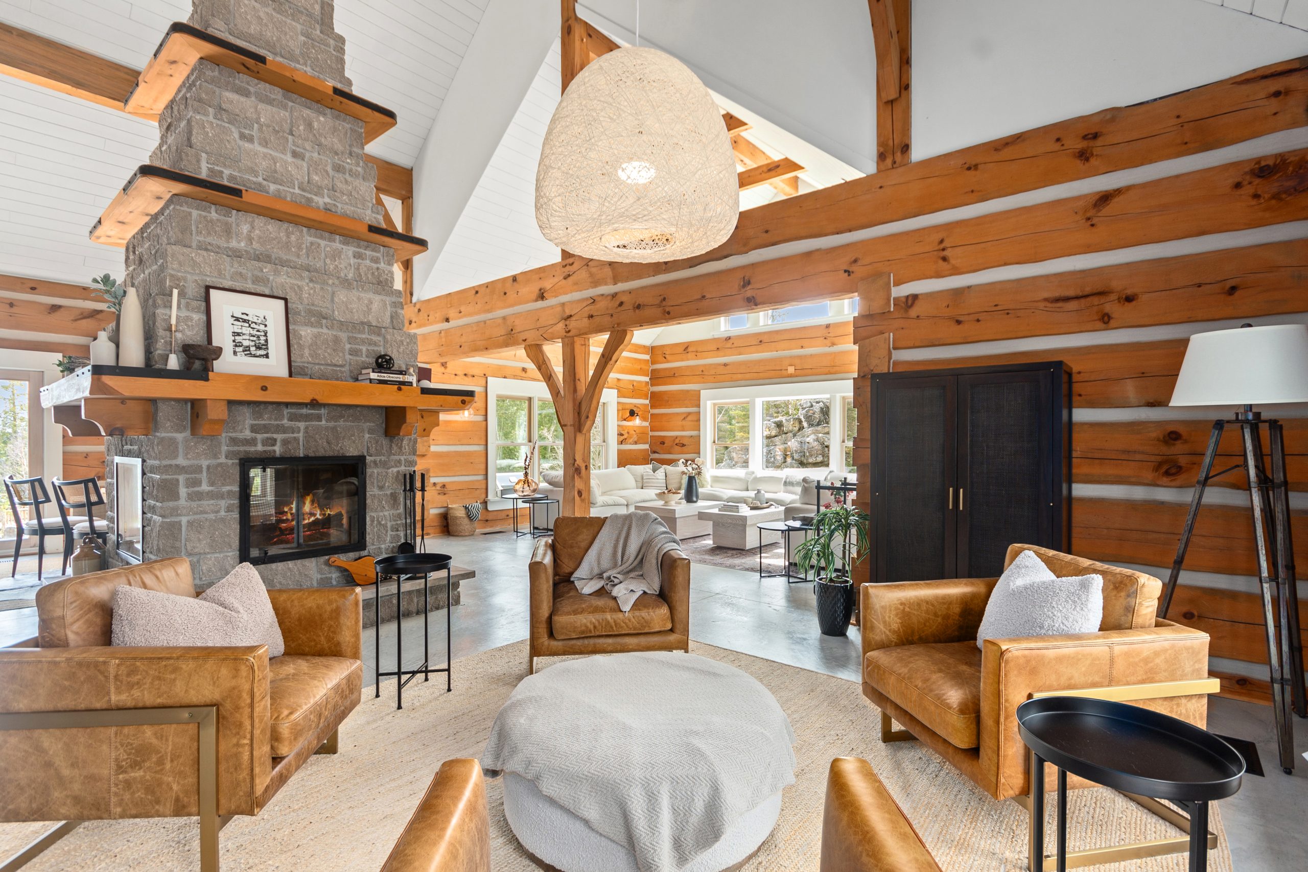 Open-concept living area with a stone fireplace, exposed wood beams, and seating arranged for gathering.