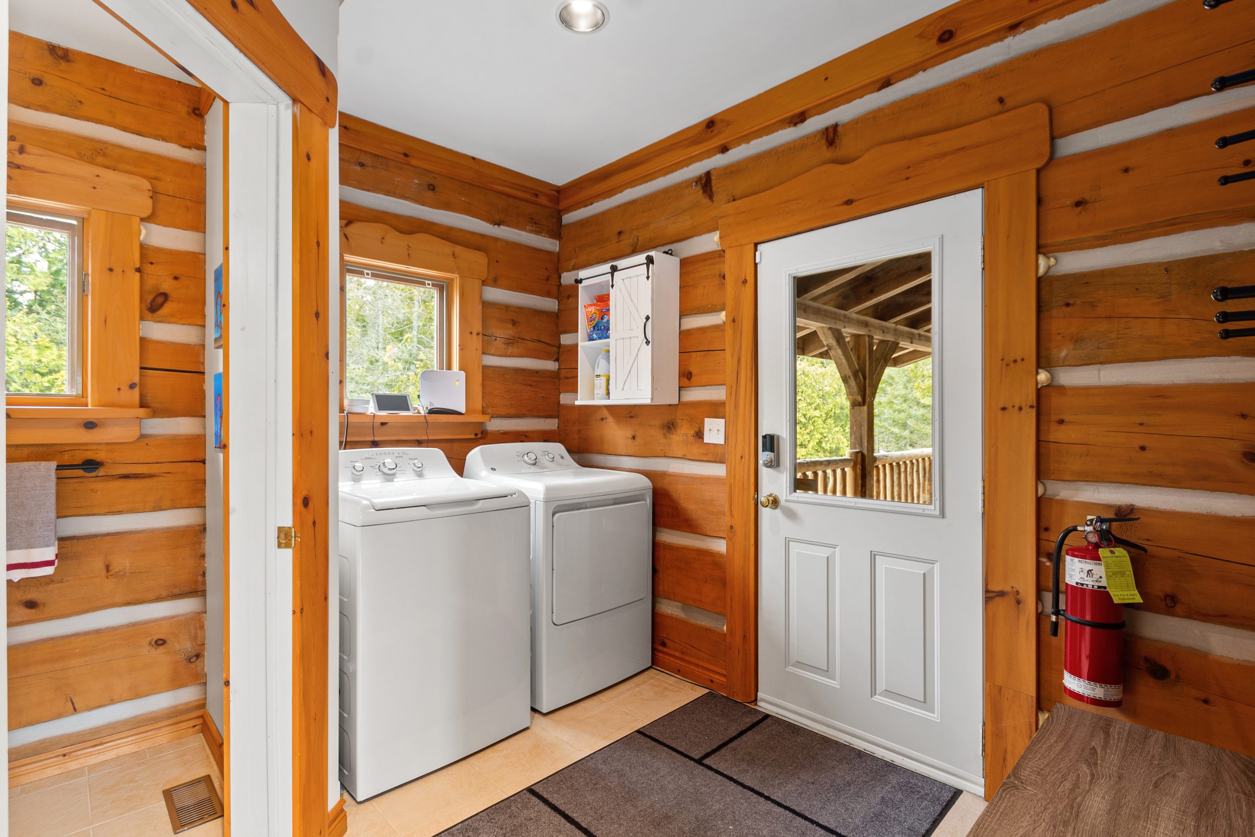 Entry/mudroom area with laundry machines, log walls, and a door leading outside.