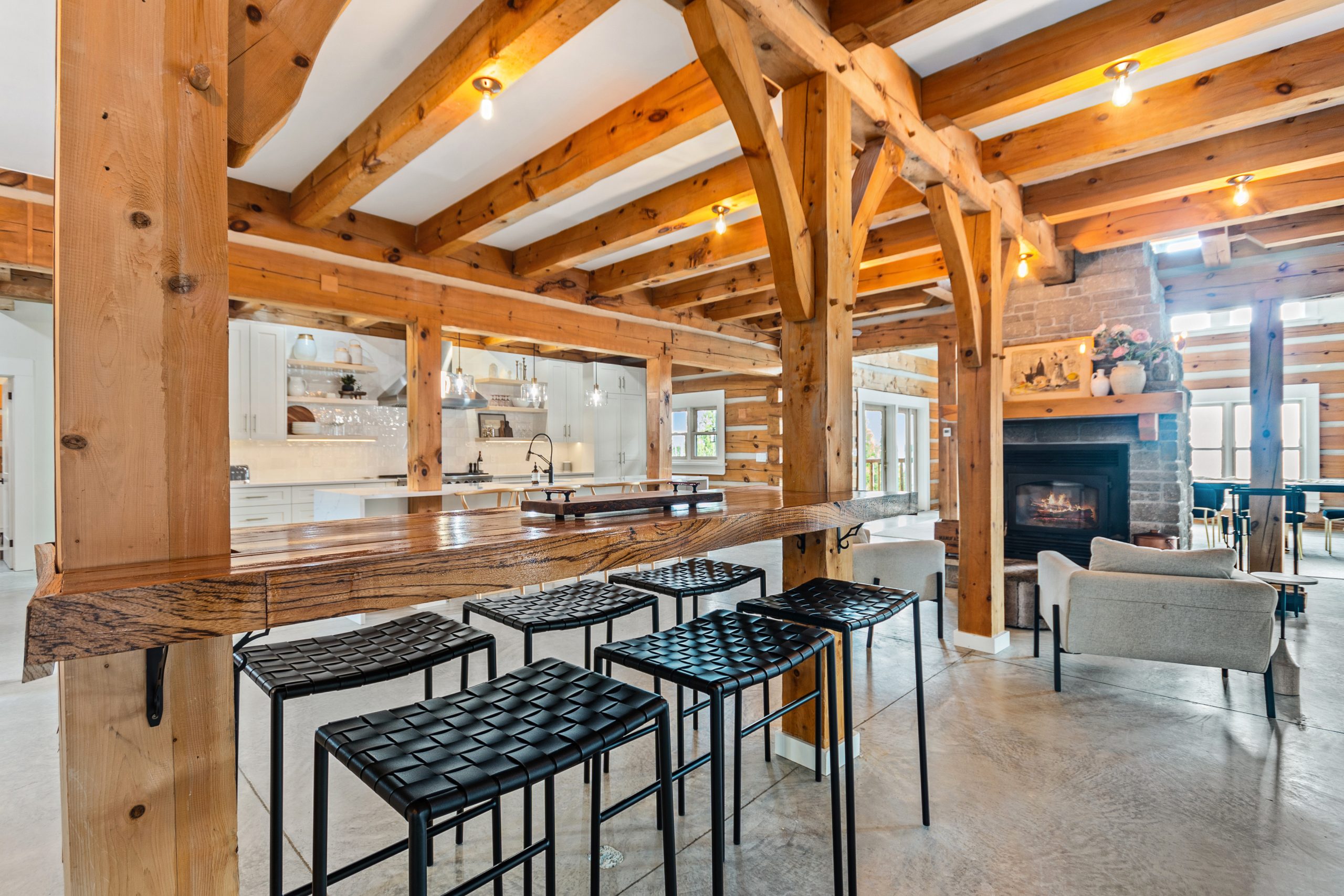 Open-concept space with a bar-height counter and stools, exposed wood beams, and a lounge area beyond.