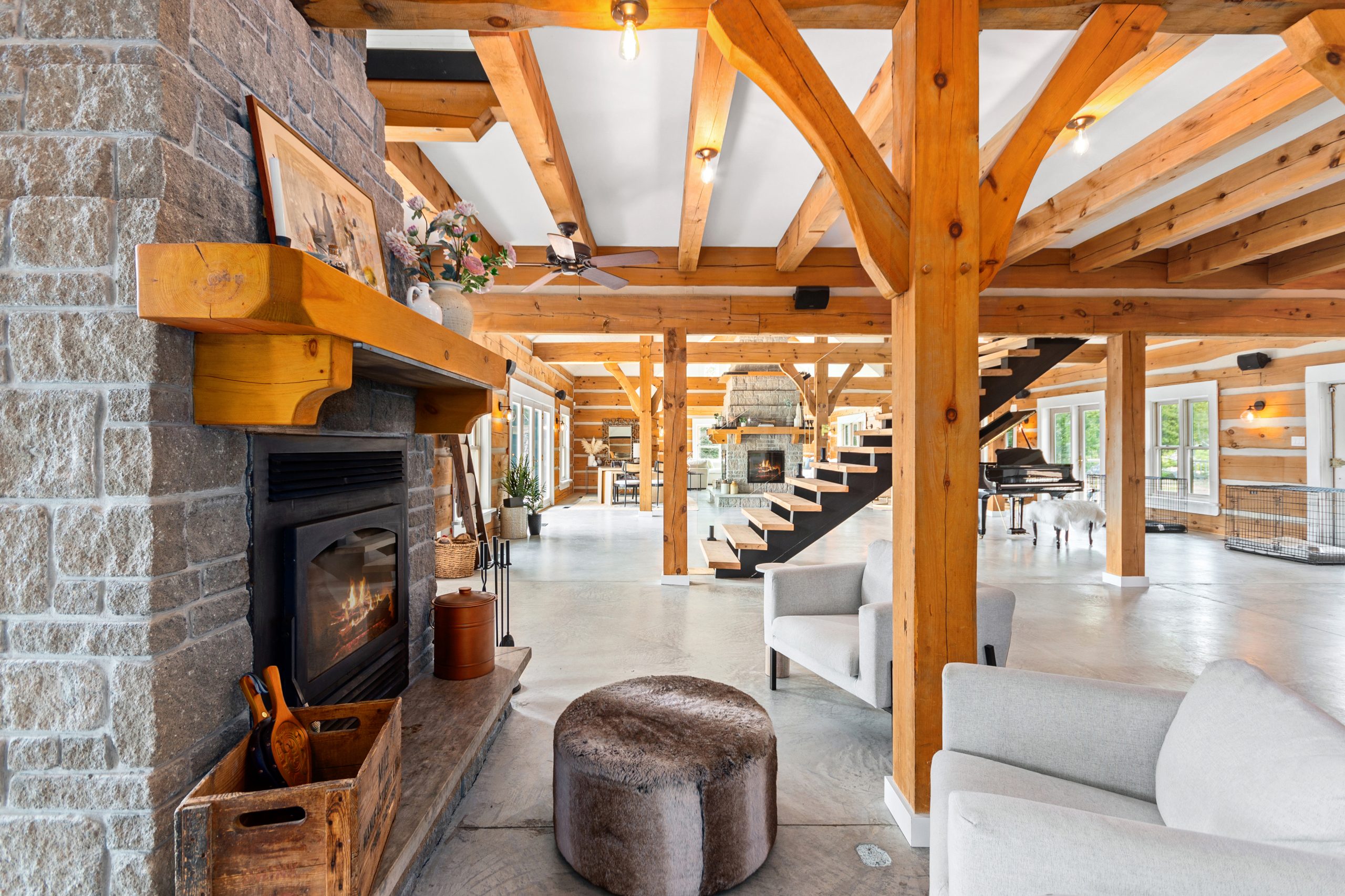 Stone fireplace and mantel in the lodge, looking into a bright open-concept interior with timber beams and seating.