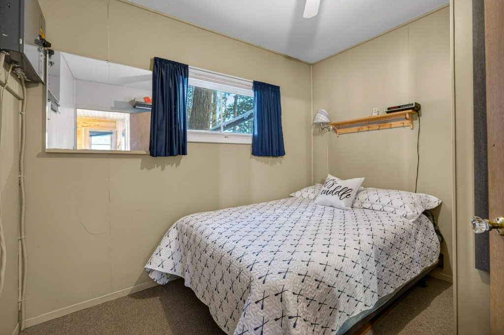 Small guest bedroom with double bed, beige walls, window, and wall shelf.