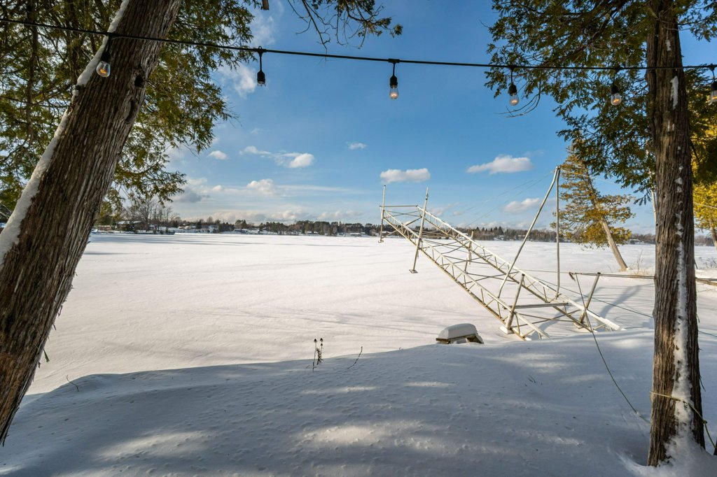 Snowy lakeside view framed by trees, with a dock extending onto the frozen lake.