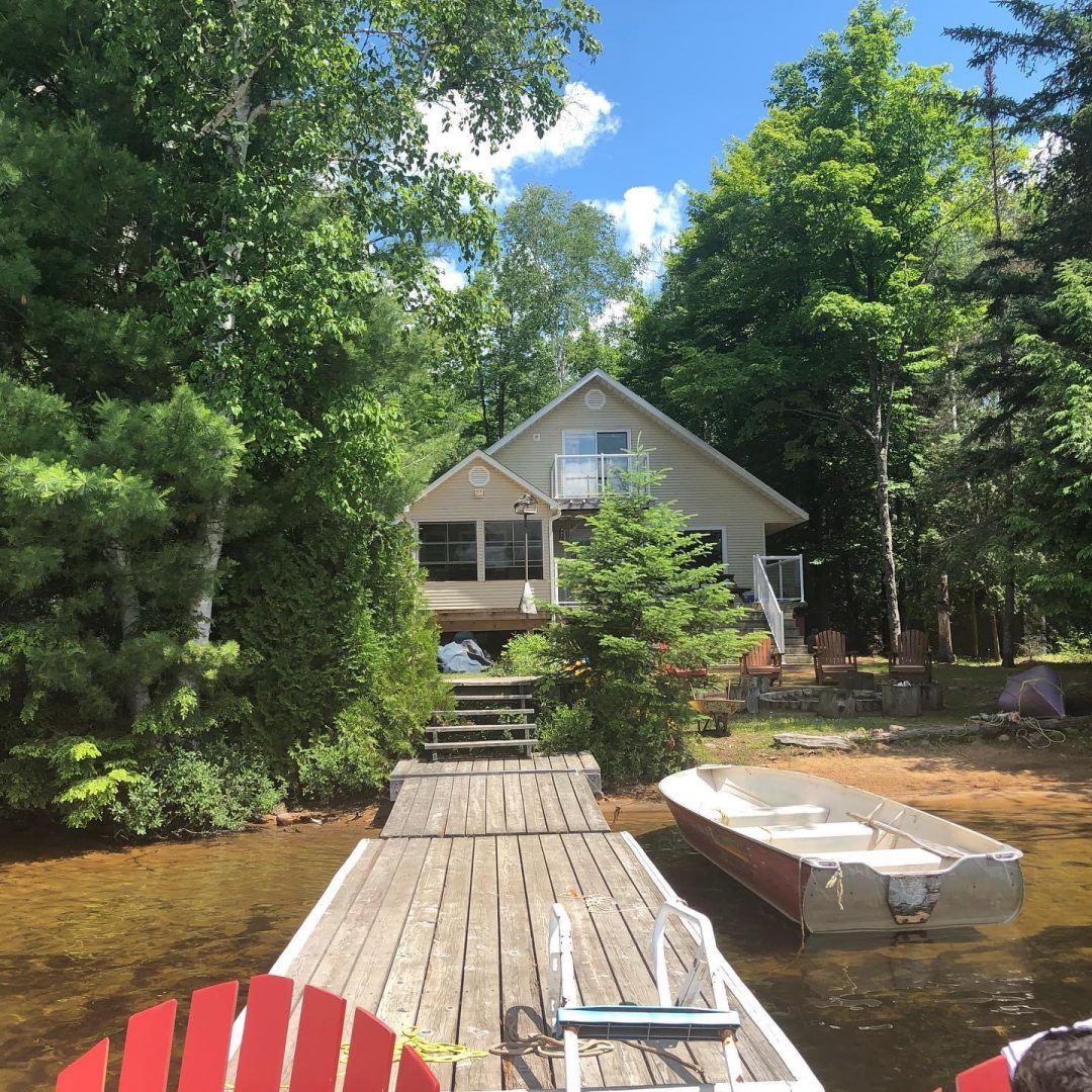 A wood dock juts out from a cottage property with a two-story wood cottage