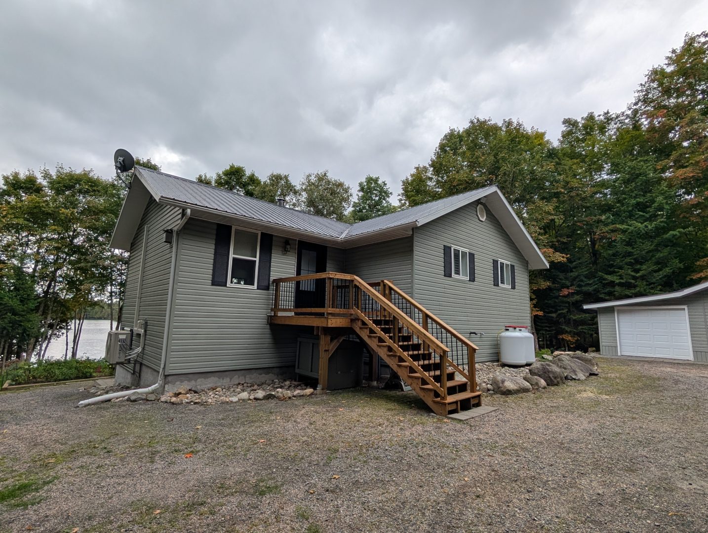 A green-grey cottage with wood steps leading to a door on a dust driveway