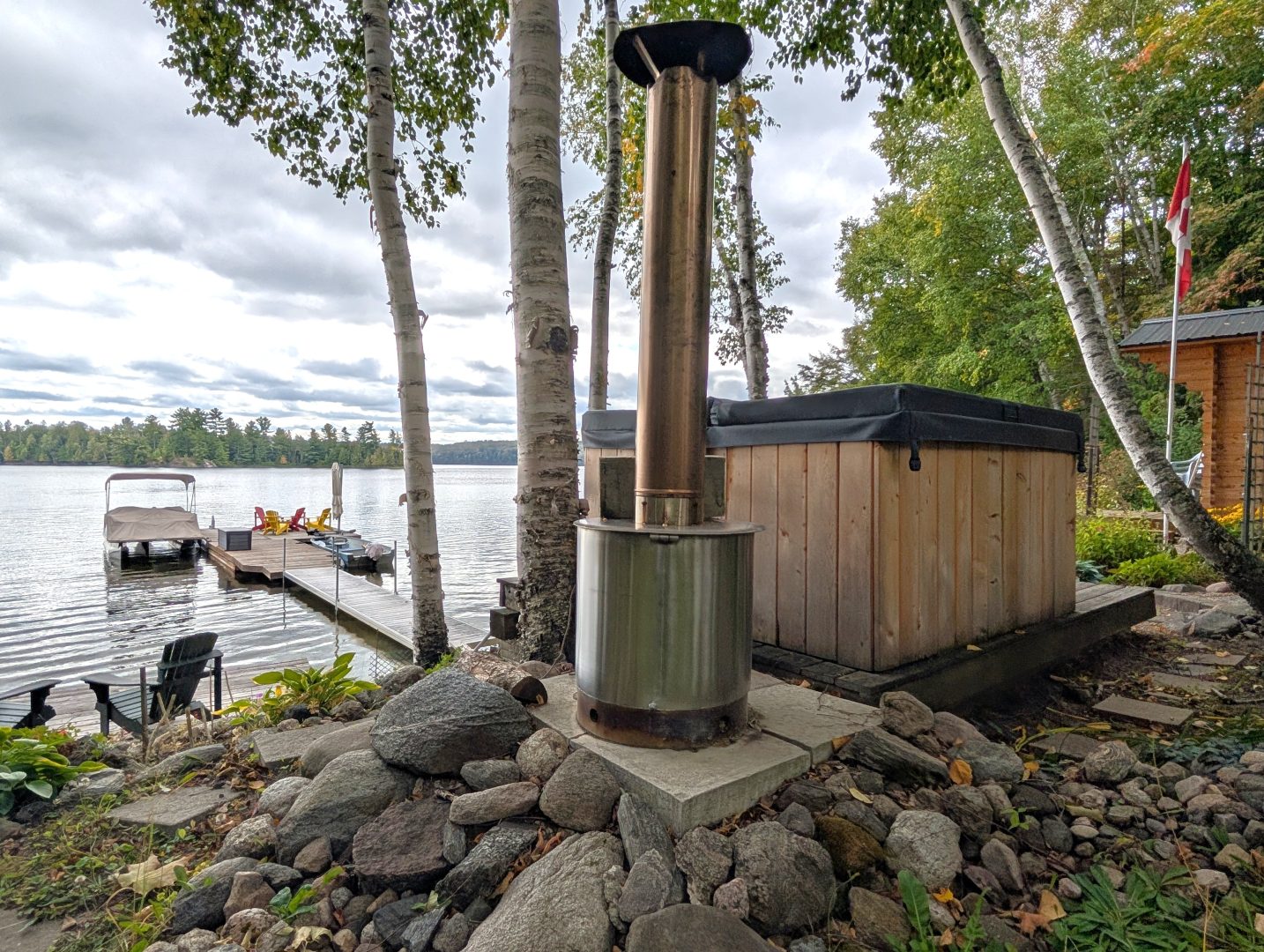 A closed wood hot tub next to a metal heater by the lake