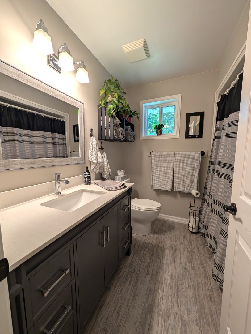 A narrow grey bathroom with a dark wood vanity