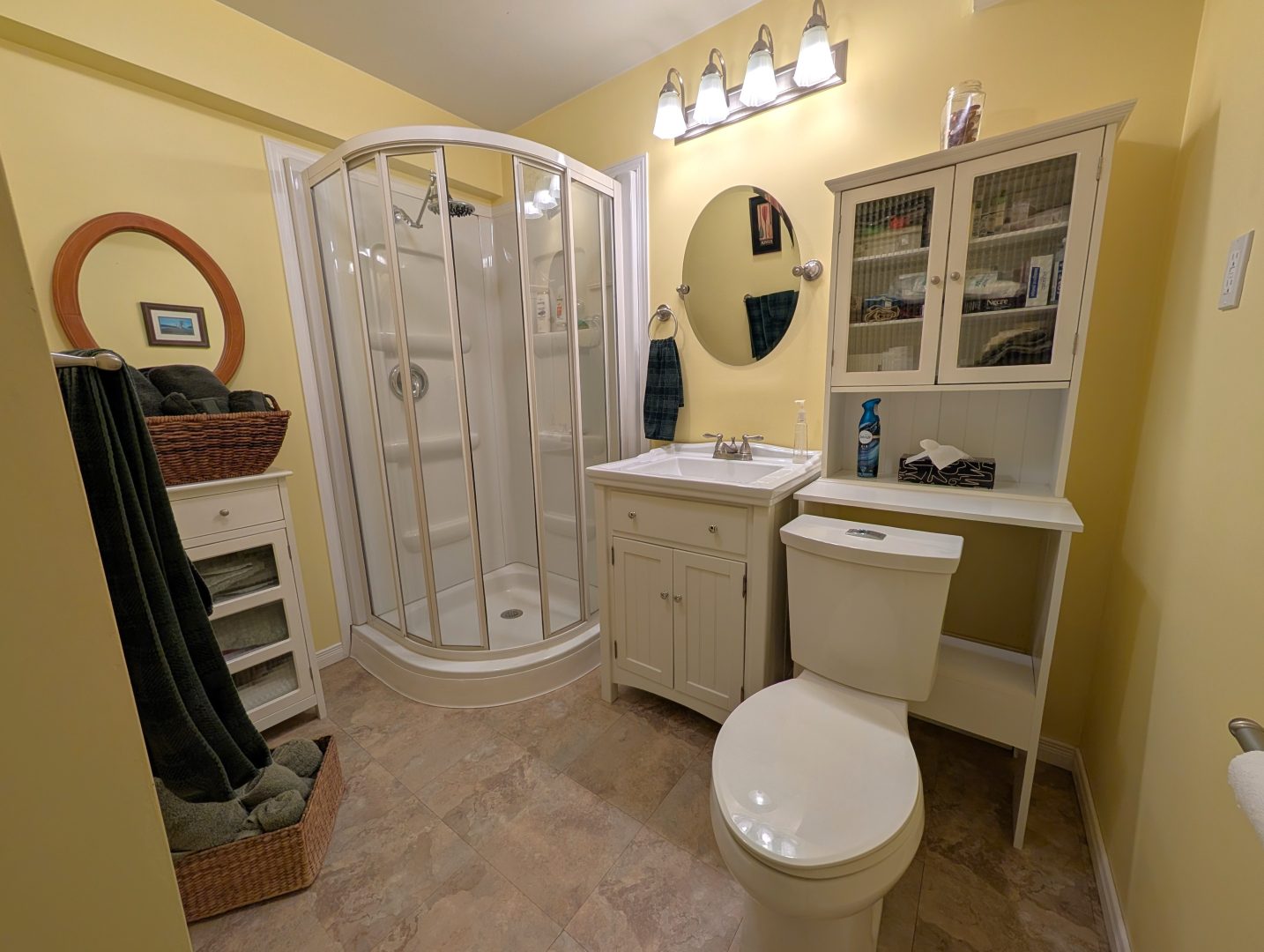 A pale yellow bathroom with a glass shower in the corner. To the right, a white vanity and white cabinetry