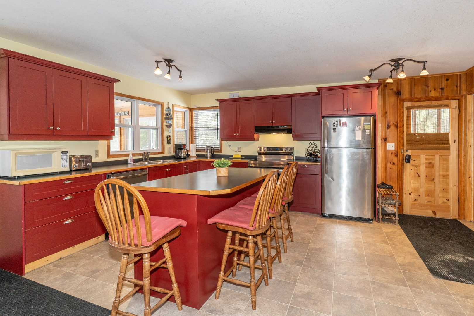 A kitchen with a reddish-brown island and tall wood chairs surrounding it