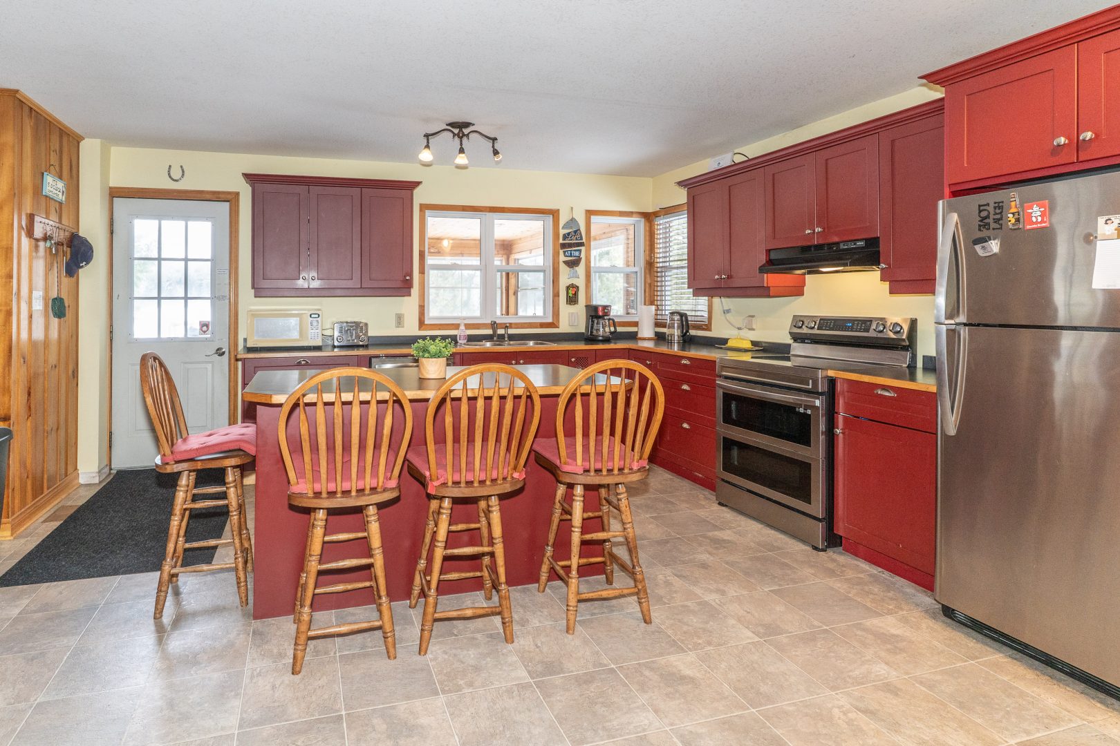 High-back wood chairs line the reddish-brown kitchen island. Red-brown cabinetry line the walls in an L-shape