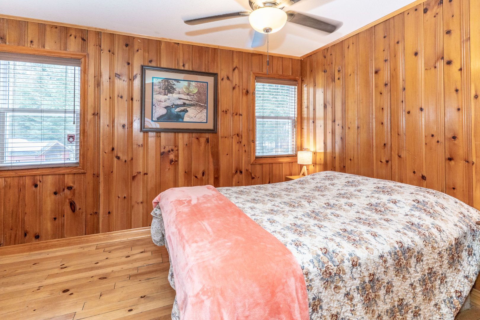 A patterned bedspread with a pink throw blanket in a wood-paneled room