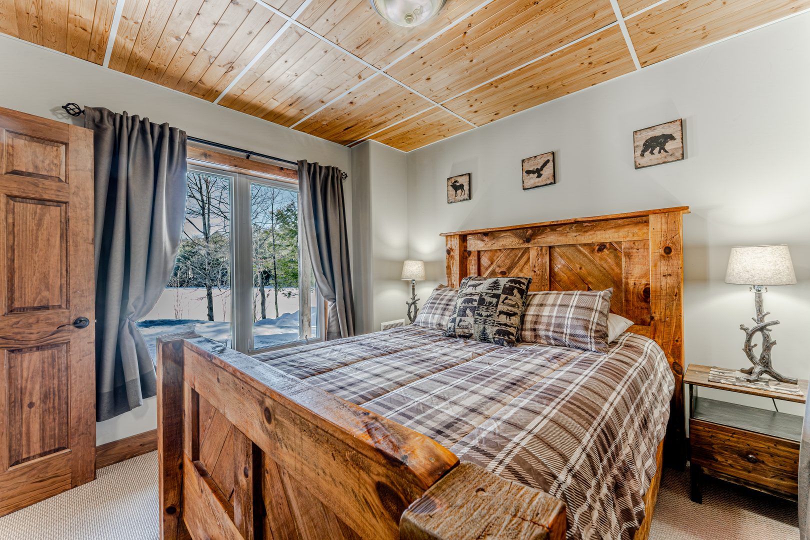 A brown and white plaid bed on a large wood bed frame next to bright windows