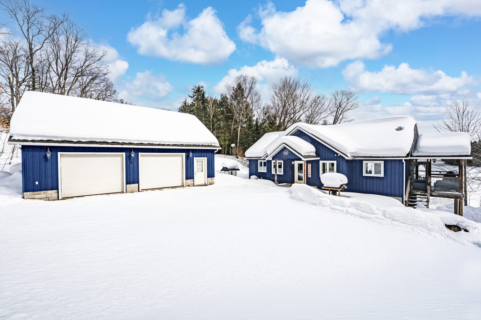 A blue two-car garage next to the blue cottage covered in snow