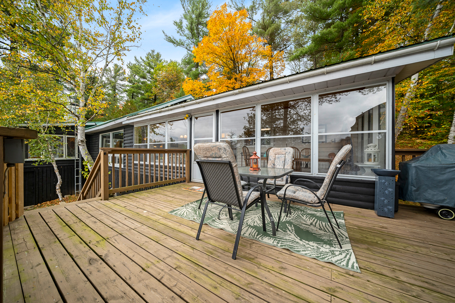 A dining area on a deck next to a glass-paneled cottage