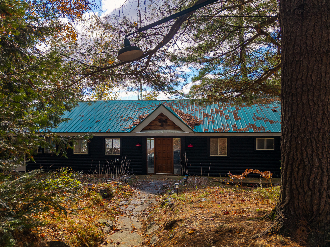 A dark blue bungalow cottage with a teal roof and a light brown door