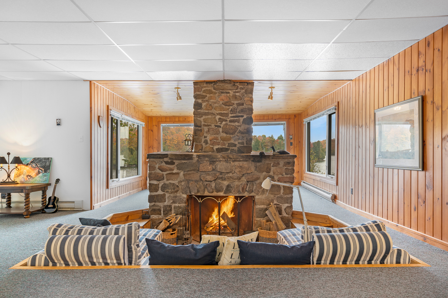 A stone fireplace and a couch with blue-and-white striped cushions are set into a wood-framed conversation pit