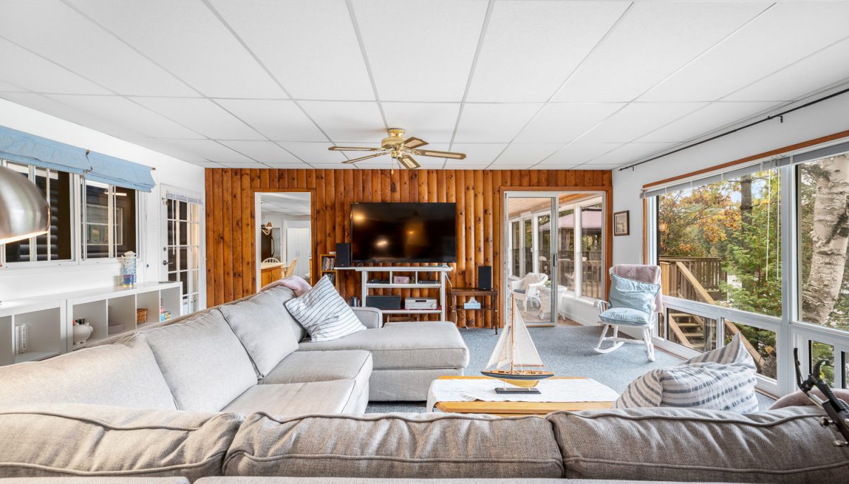 L-shaped beige couches face a wood-paneled wall with a TV in a sunny room