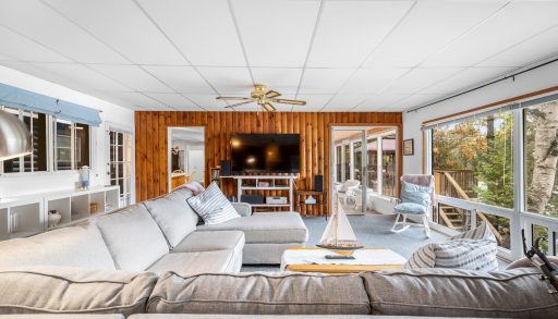 L-shaped beige couches face a wood-paneled wall with a TV in a sunny room