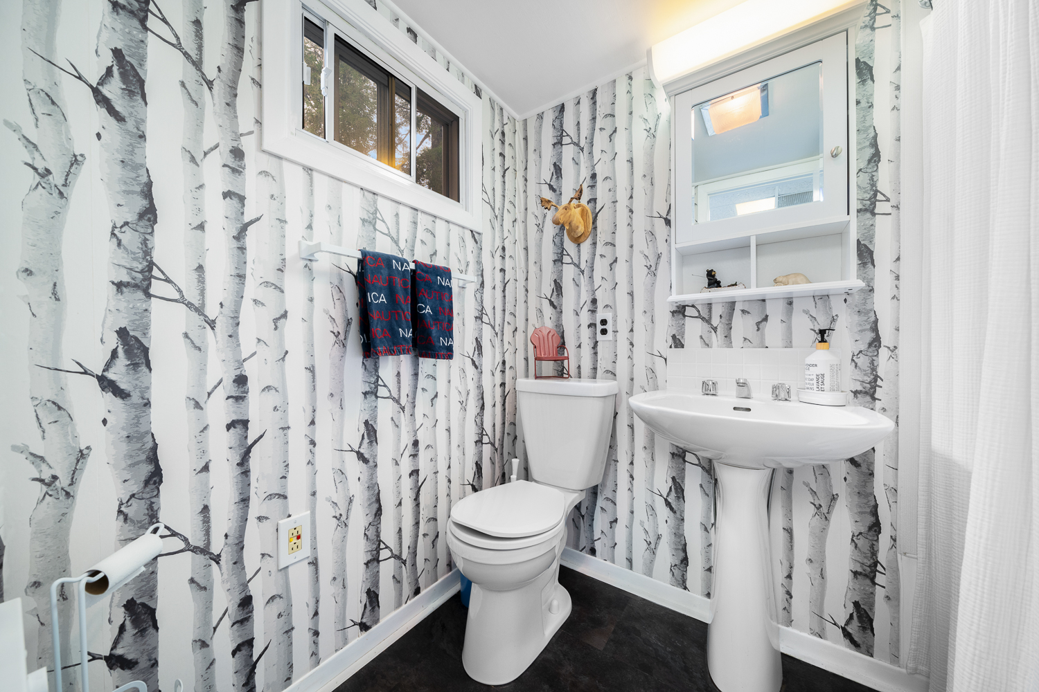 A white toilet next to a white sink in a bathroom covered in birch tree wallpaper