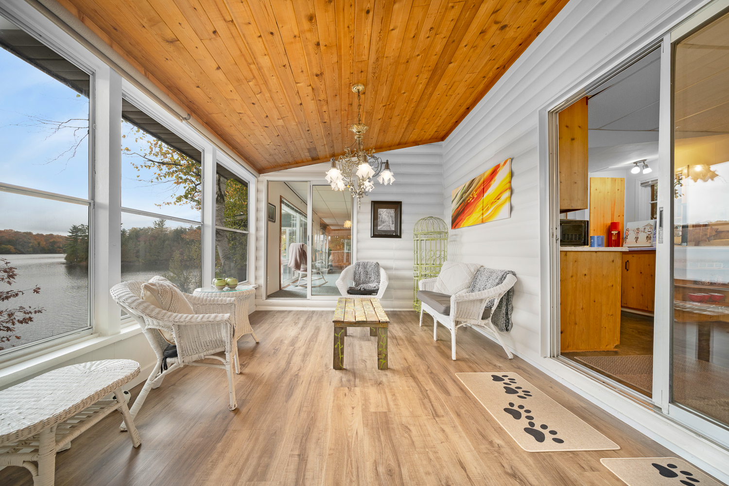 White chairs in a bright sun room with a wood-paneled ceiling and floor-to-ceiling windows