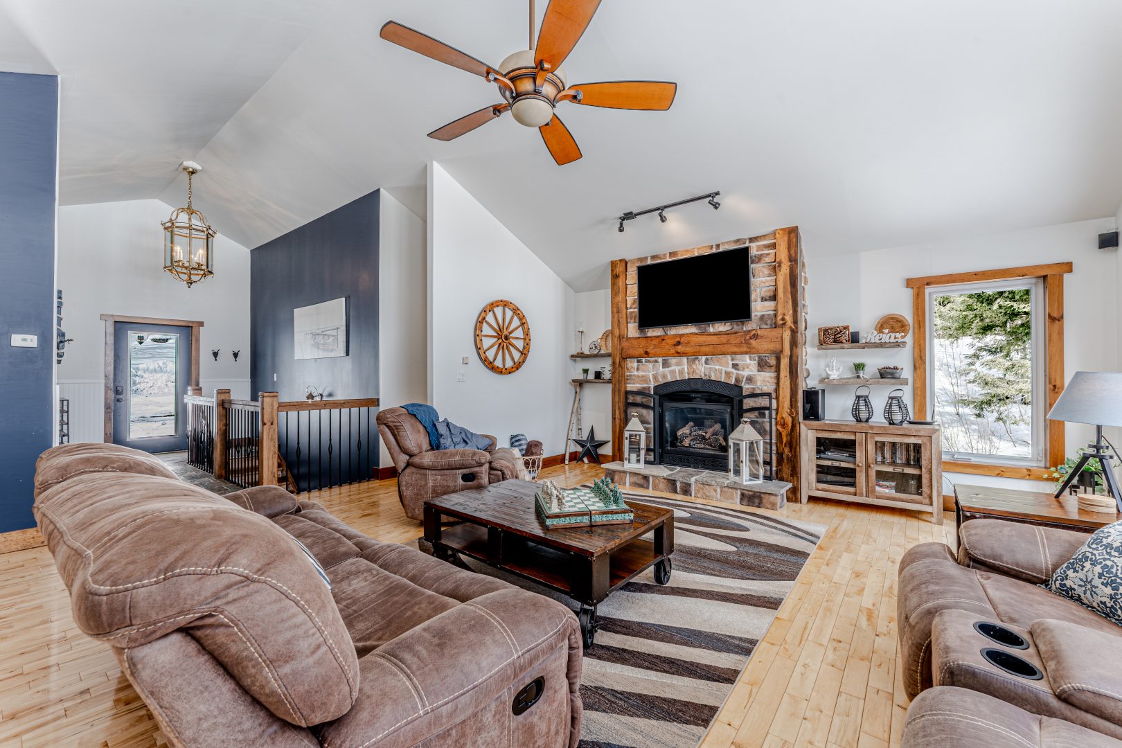 A stone and wood fireplace faces an oversized brown couch in a spacious living room