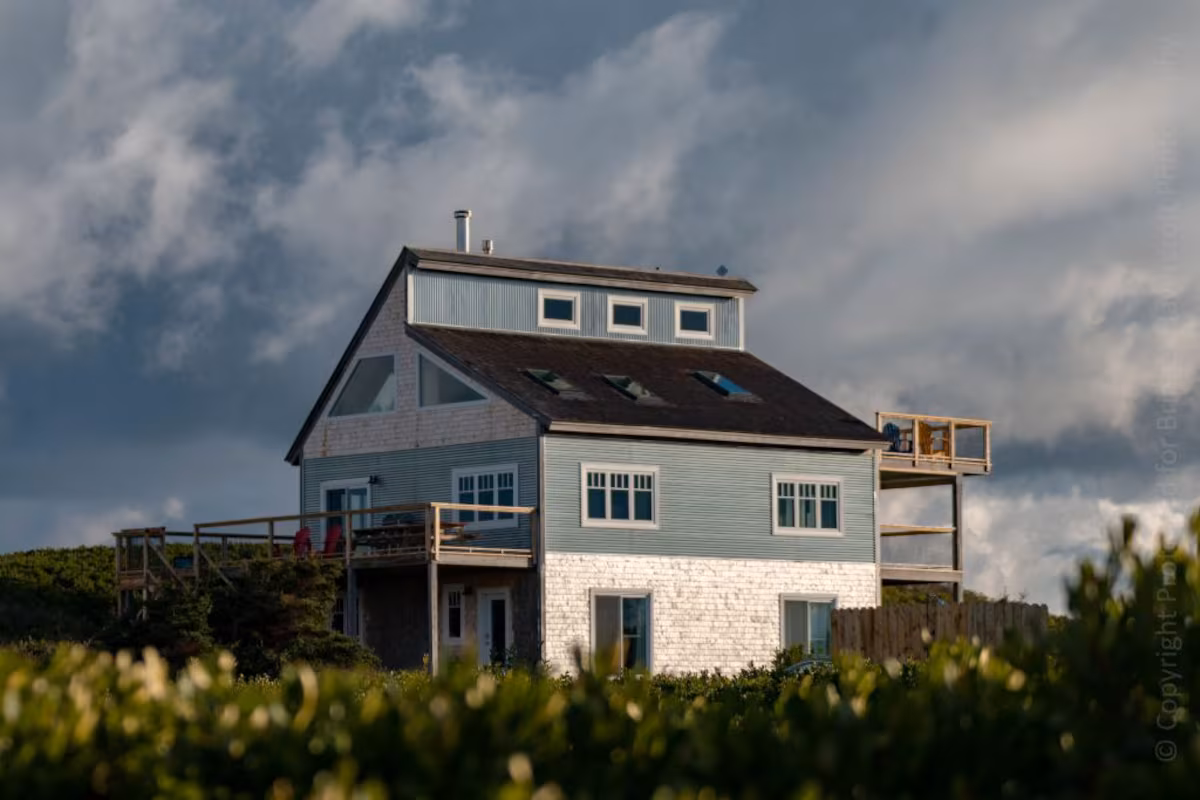 Exterior of sea dunes beach house. The home has a black roof with a blue and white exterior