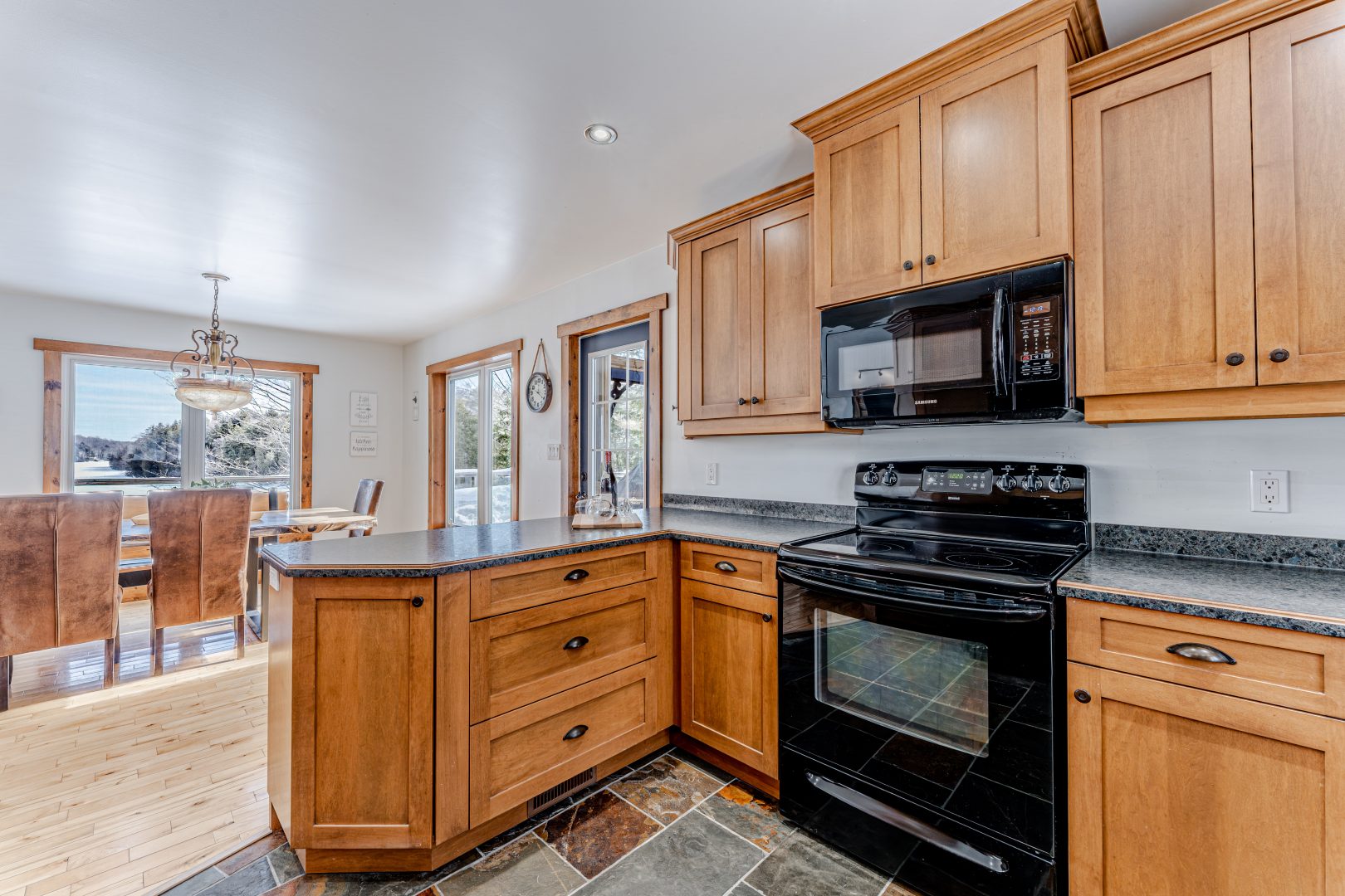 A small kitchen with brown cabinets, black appliances, and a stone floor