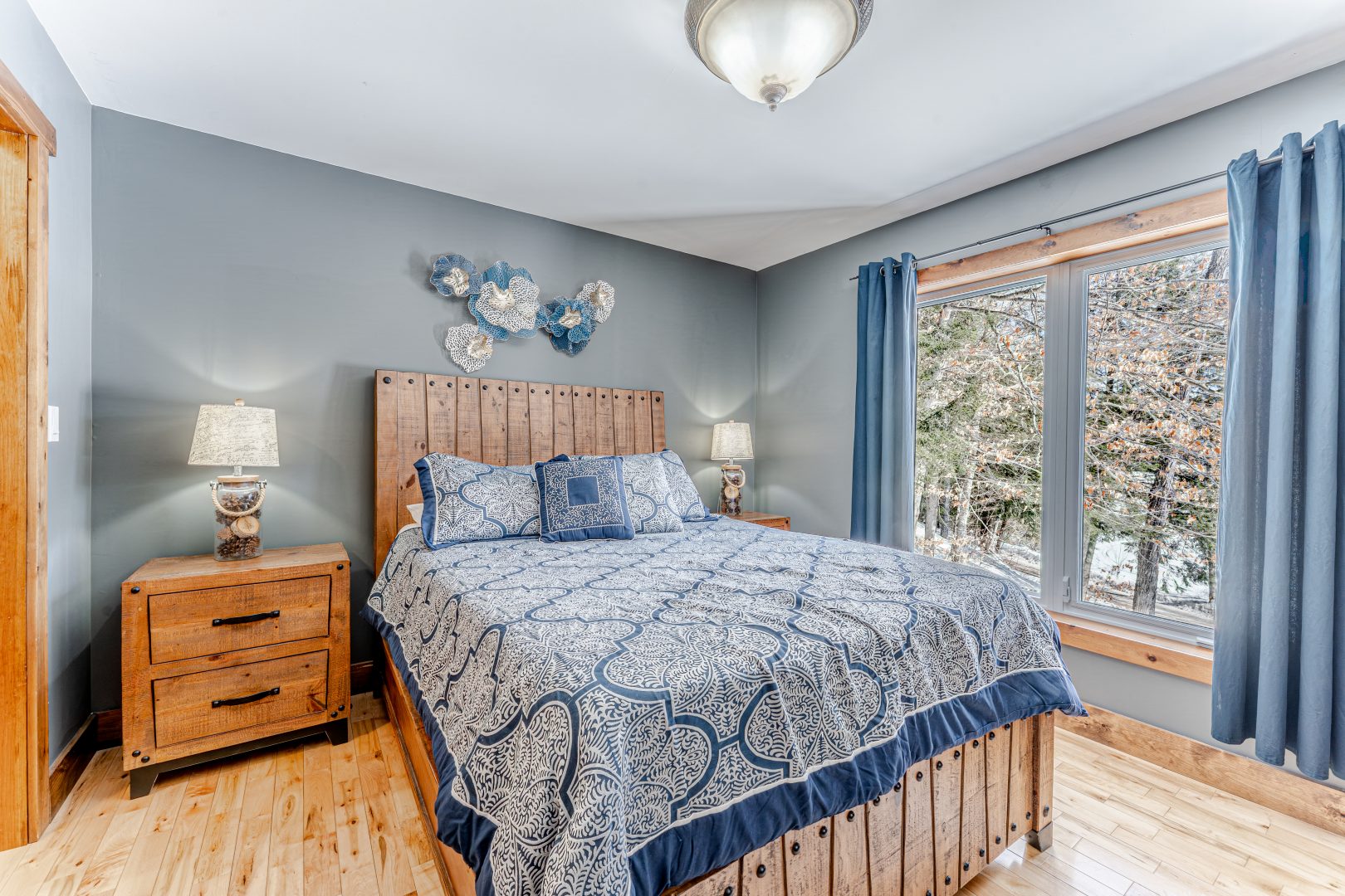 A blue bed on a wood bed frame in a grey-blue bedroom