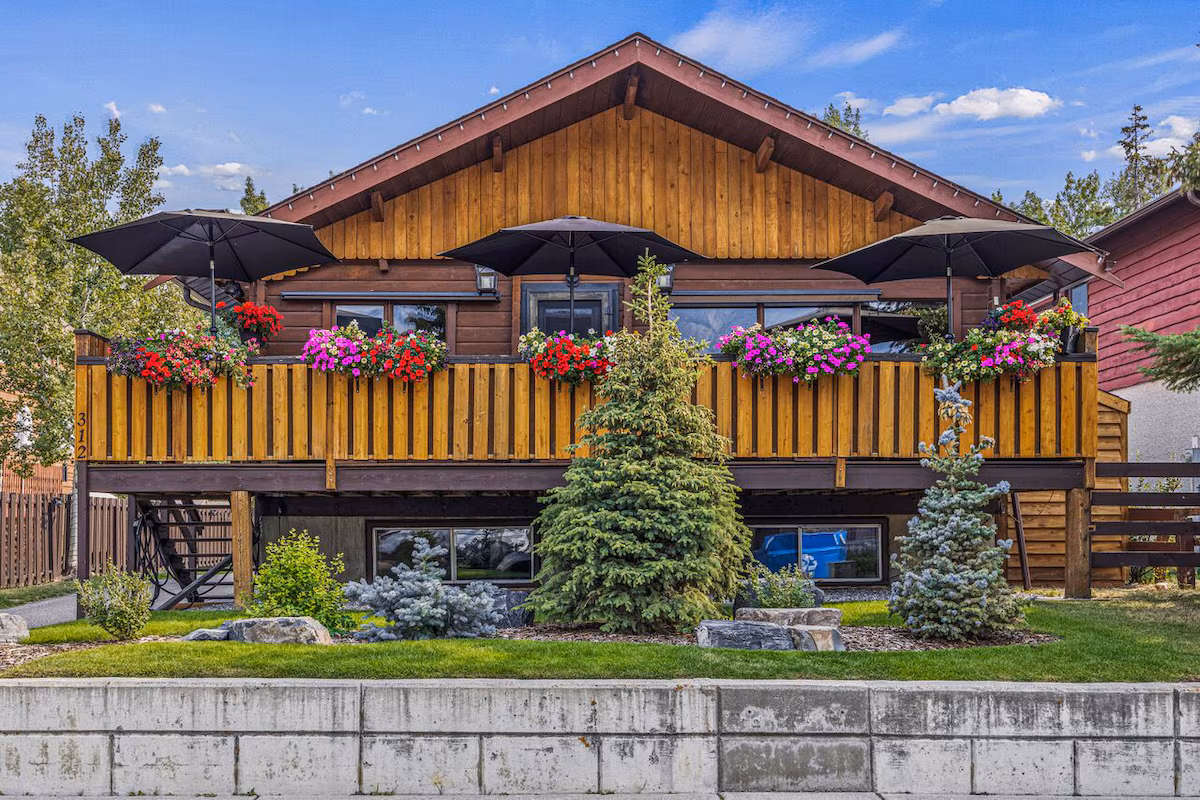 Frontal view of the rustic mountain home in Banff. The picture shows a view of the deck that has flowers on the ledge.