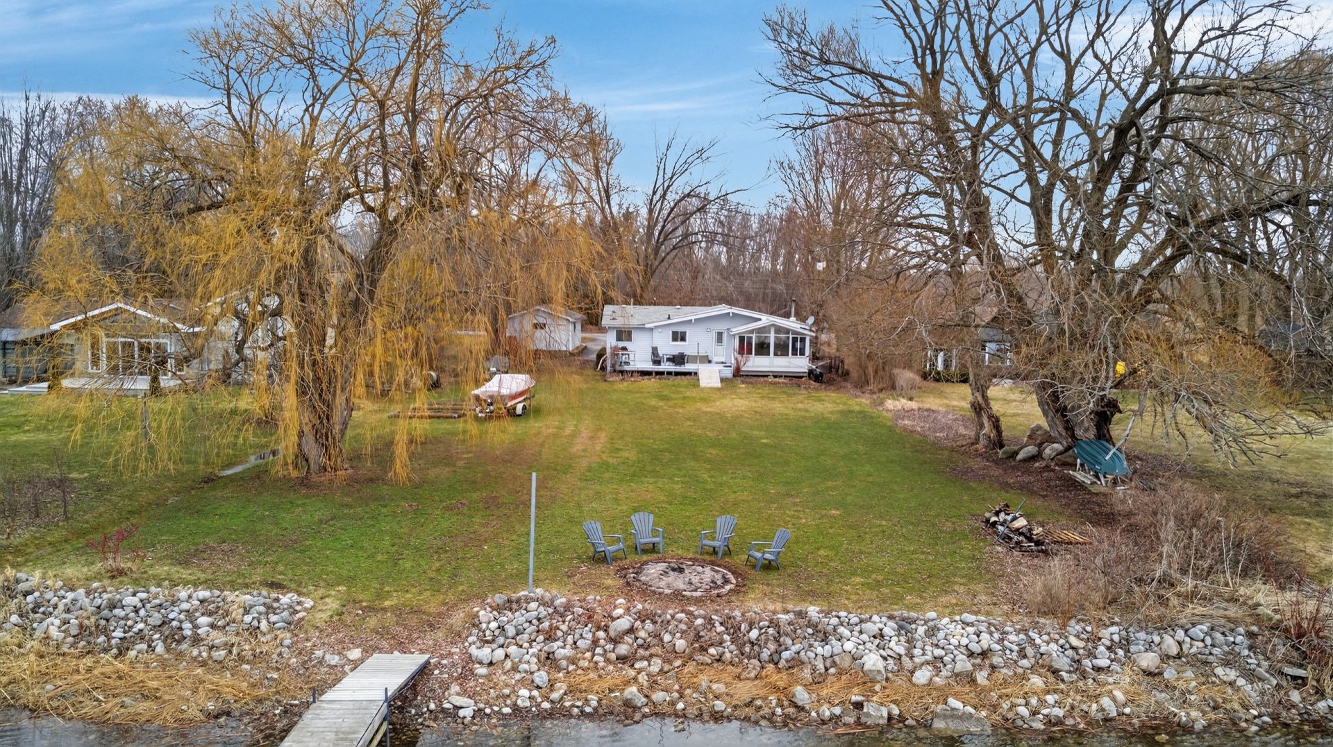 A green yard with a cottage set back. A rocky shoreline and dock jut out at the front.