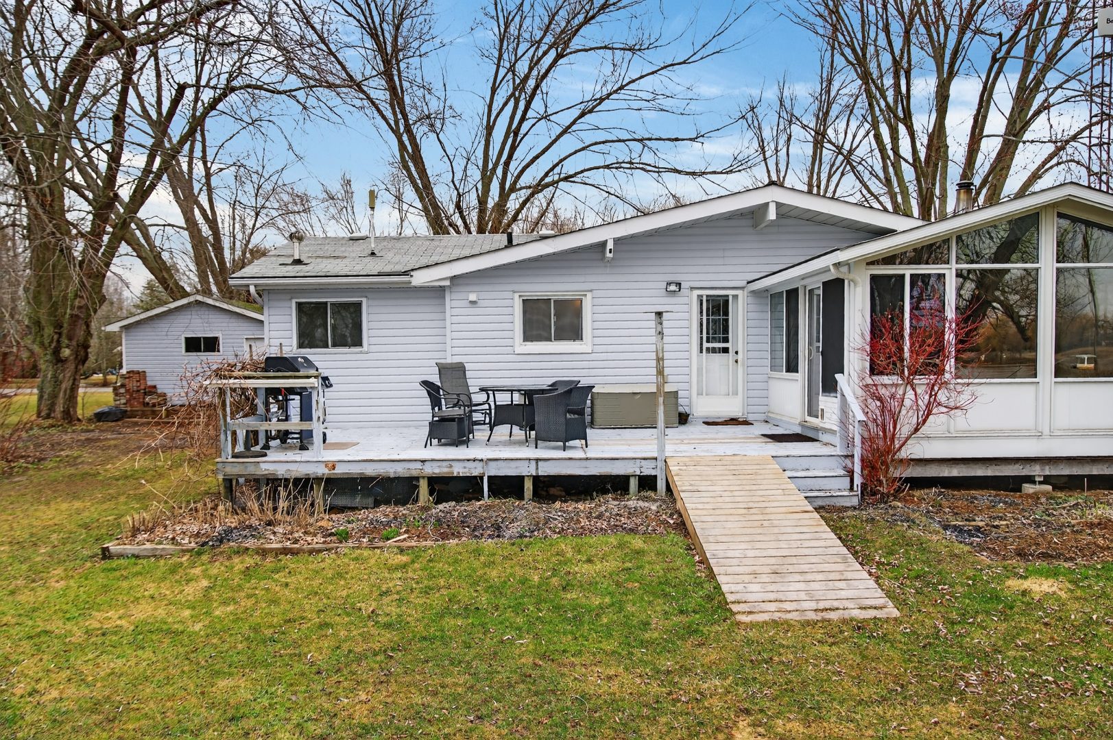 A white paneled cottage with a small deck and a ramp to the grass