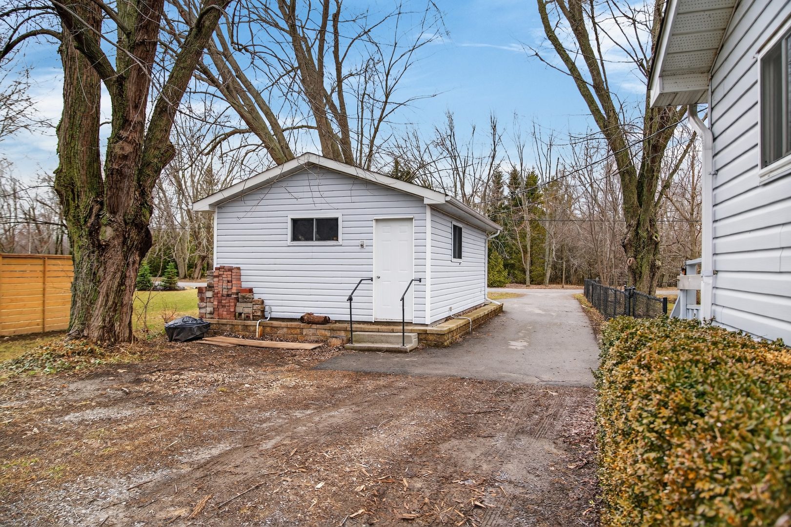 A white paneled cottage with a white door on a dirt driveway