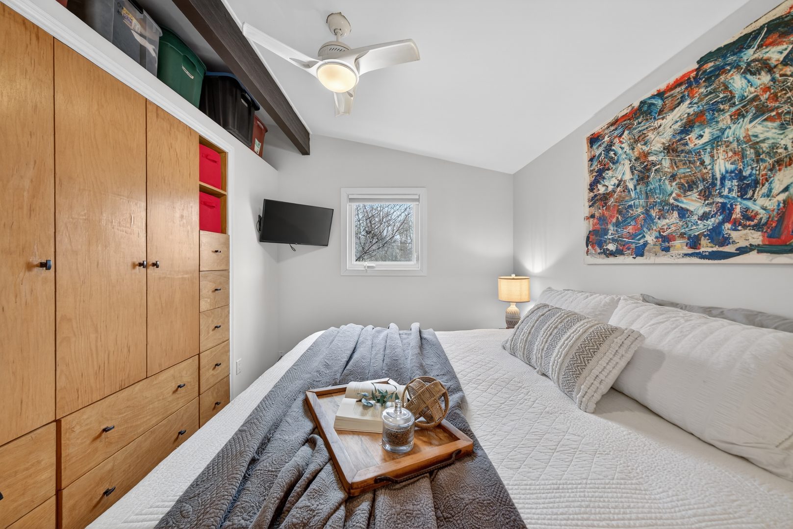 A white bed with a grey throw facing a wood paneled closet