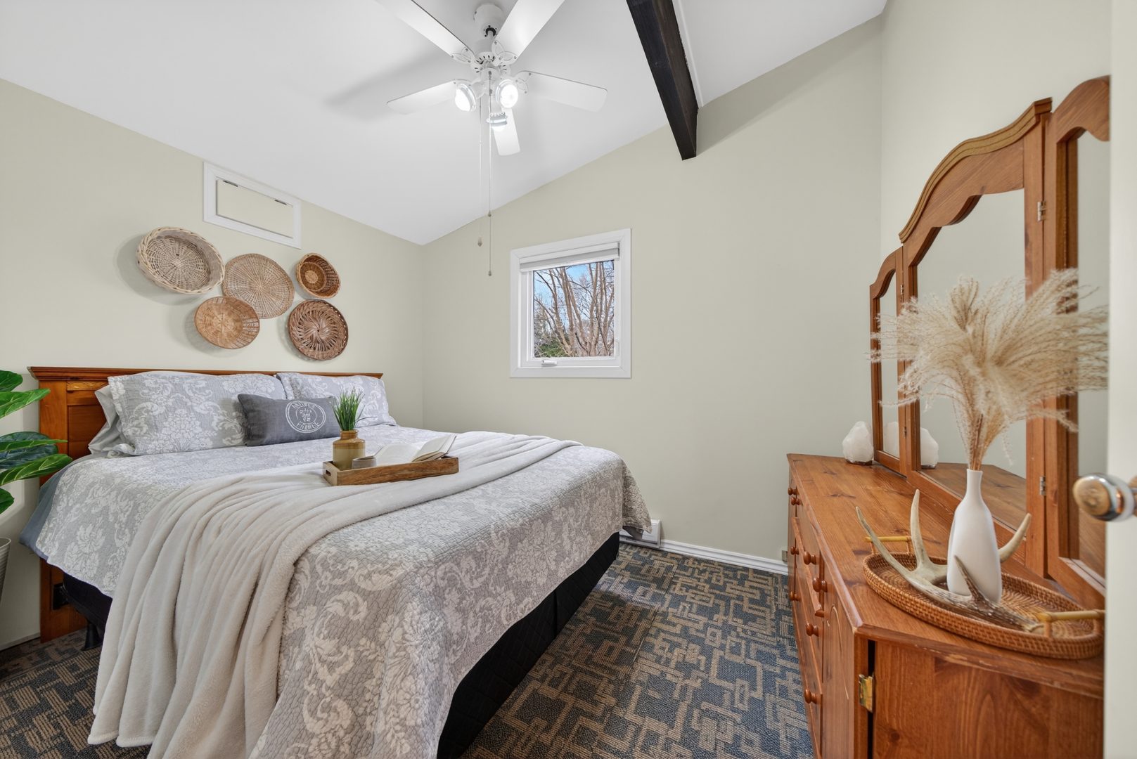 A beige bed in a white room faces a wood vanity
