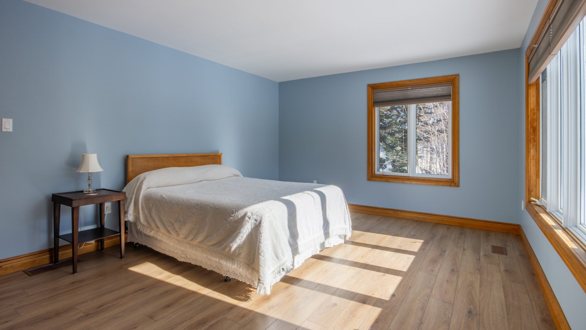 A light blue bedroom with a white bed bathed in sunlight