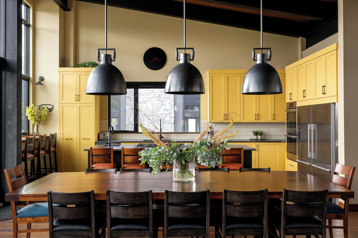 Kitchen of Nordic-inspired mountain home. This picture displays yellow painted walls and cabinets, and a brown wooden table.