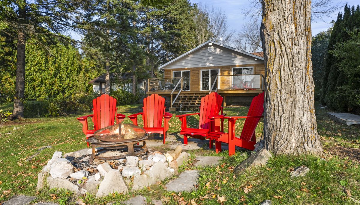 Four red Muskoka chairs by a stone fire pit on a grassy property