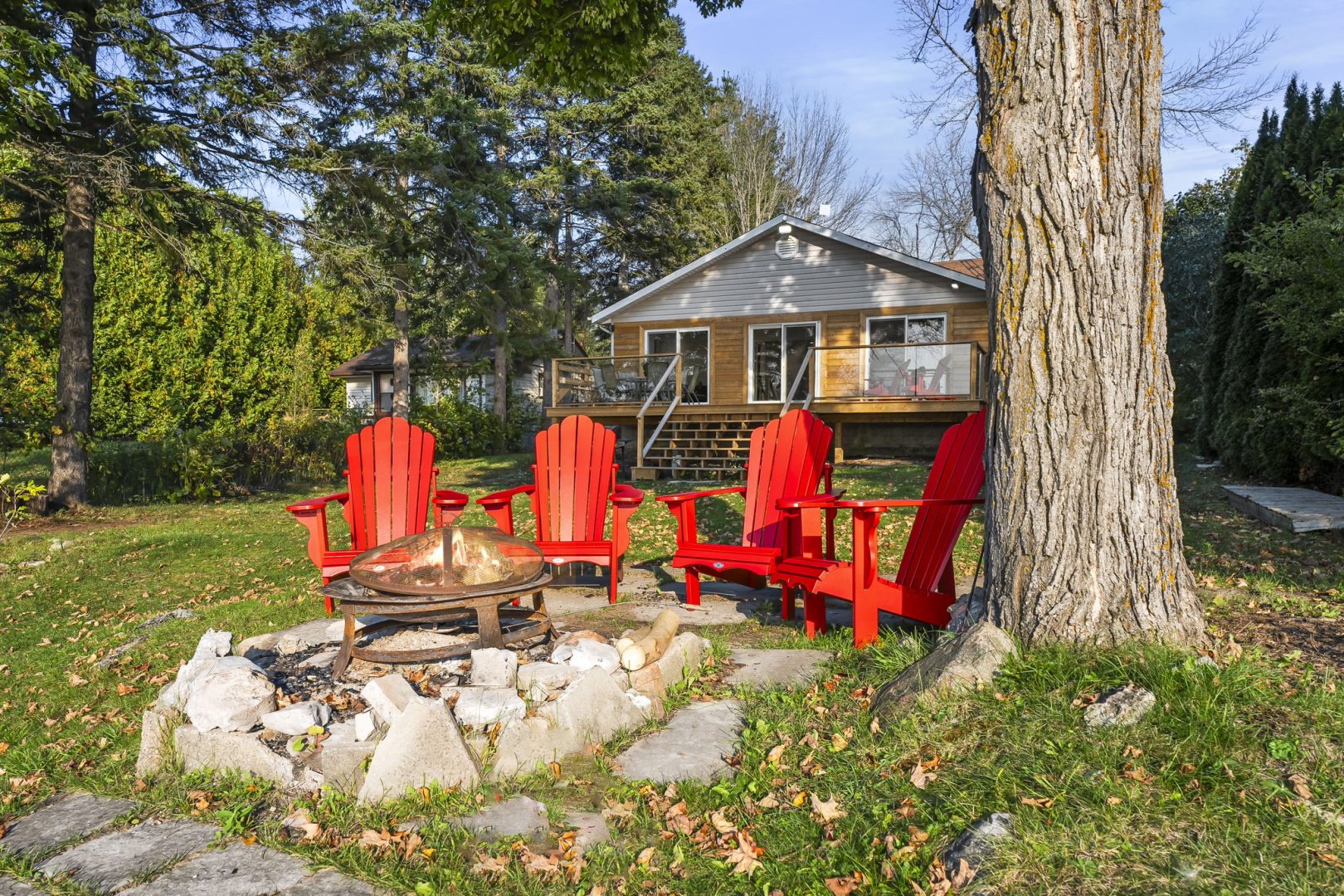 Four red Muskoka chairs by a stone fire pit on a grassy property