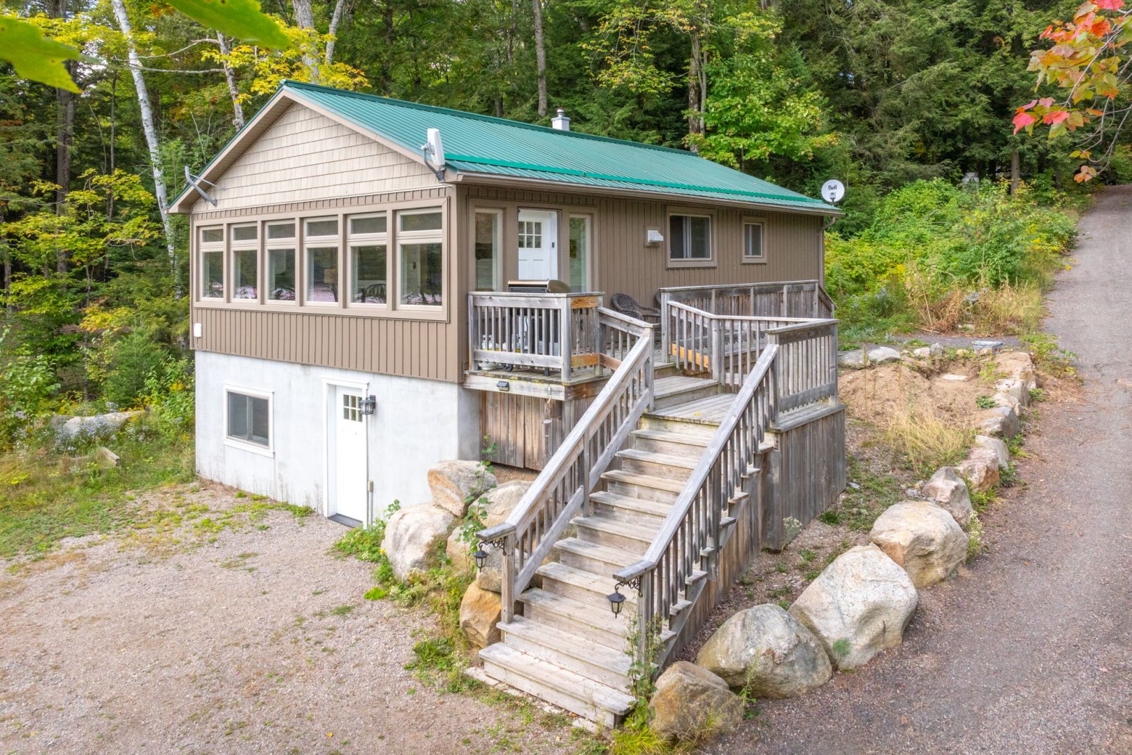 A white and brown cottage with a green roof and wood stairs to the driveway
