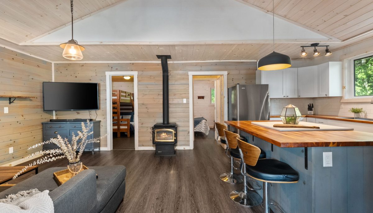 An open-concept living area with a grey couch to the left, a wood stove and a grey high-top island