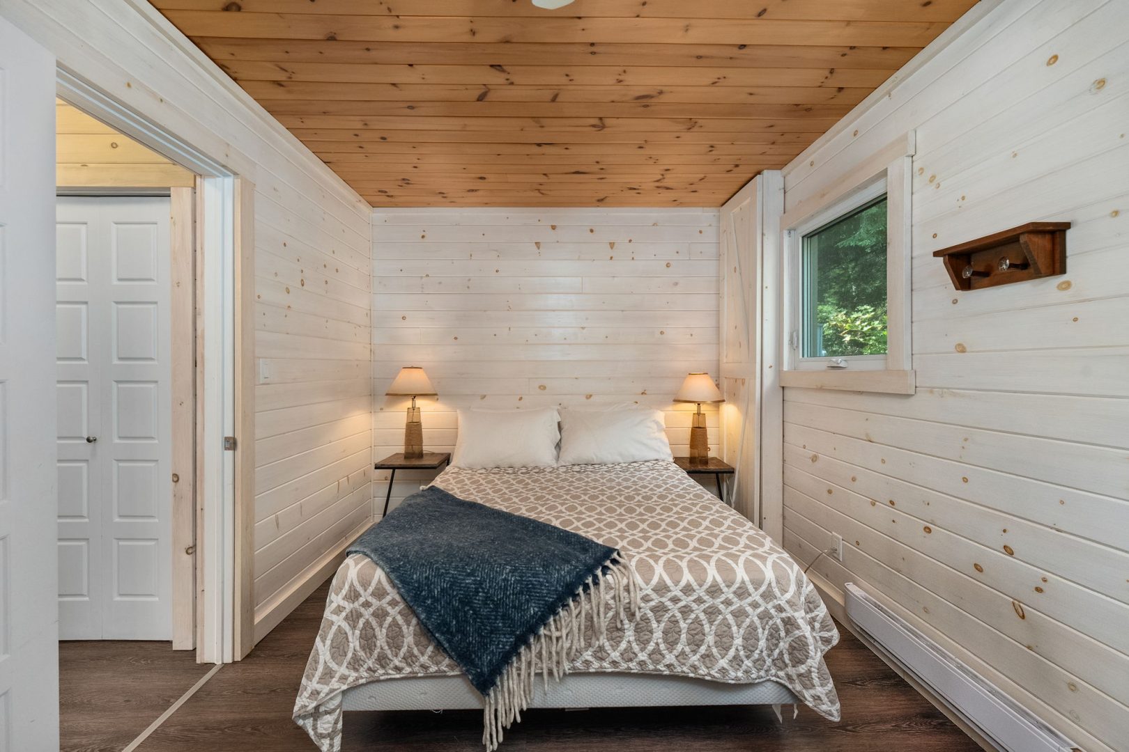 A white bed with a grey throw in a white bedroom