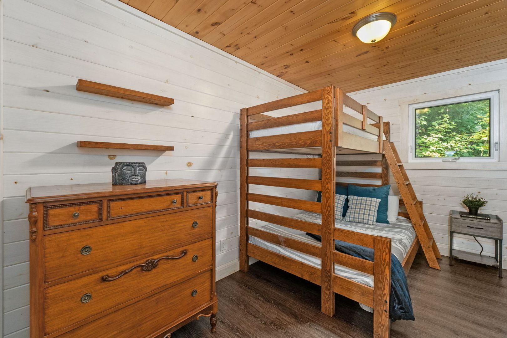 A wood bunk bed next to a wood dresser in a white bedroom