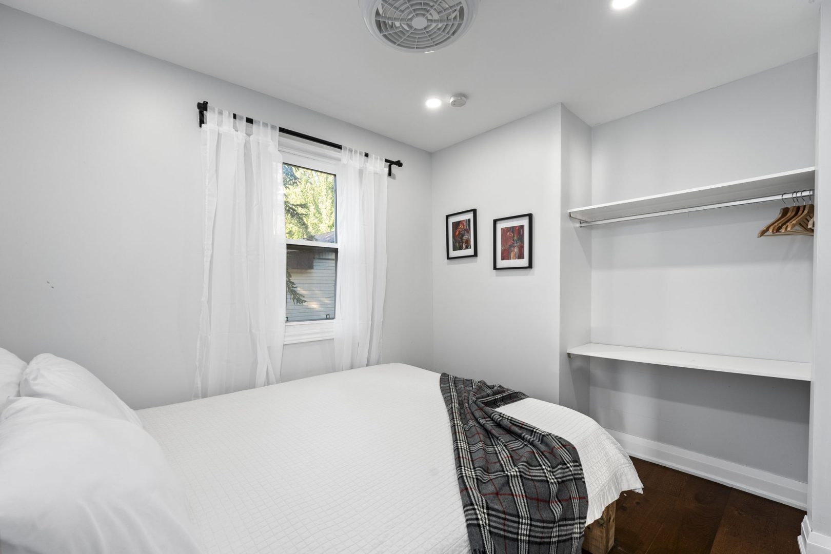 A white bed with a grey plaid throw in a white bedroom