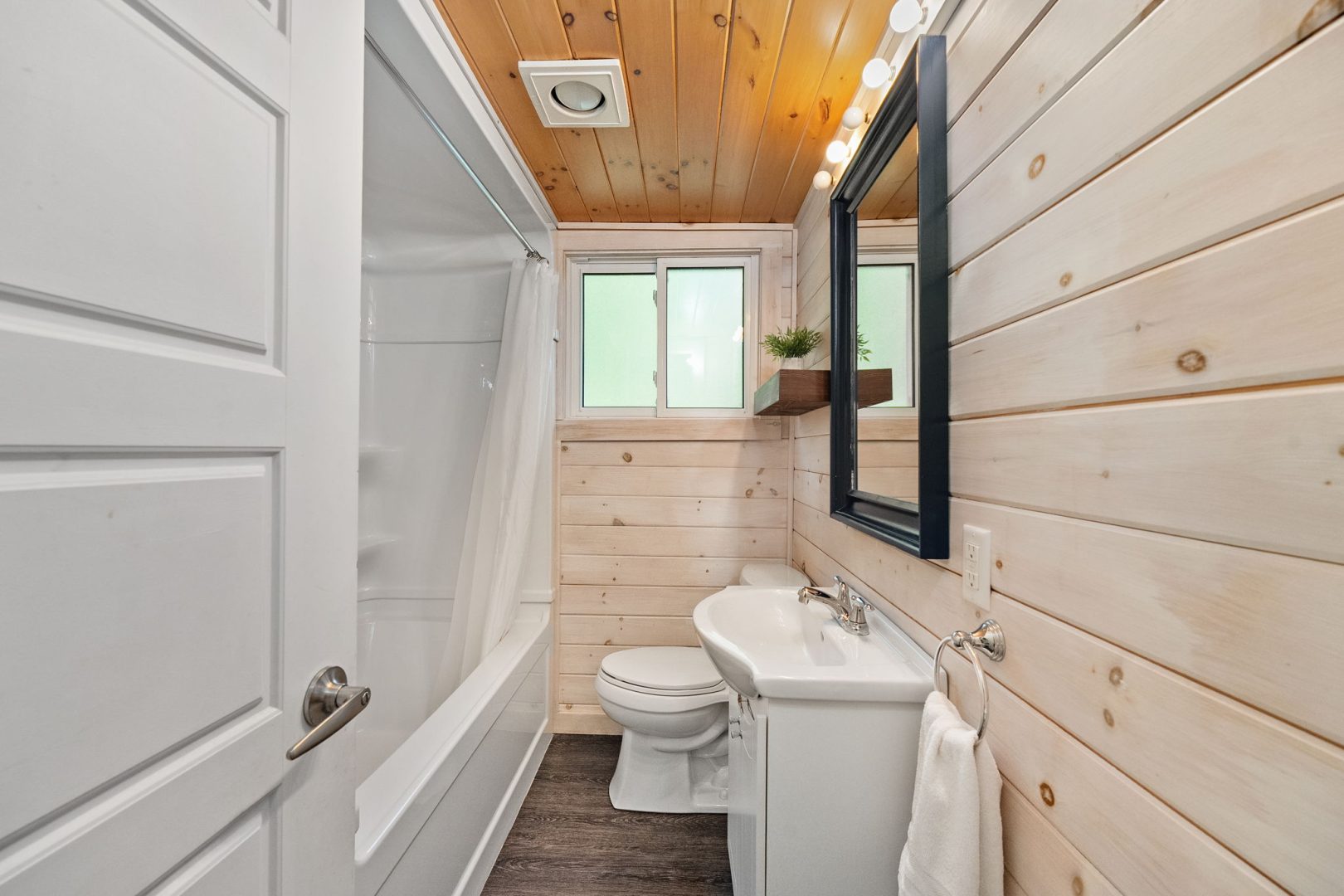 A wood paneled bathroom with a white shower facing the white vanity and tub