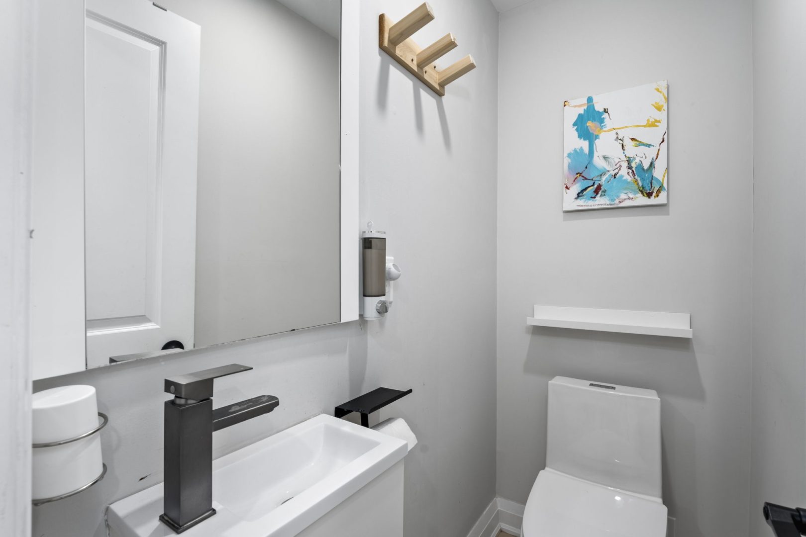 A small white powder room with a slim vanity and wood wall hooks