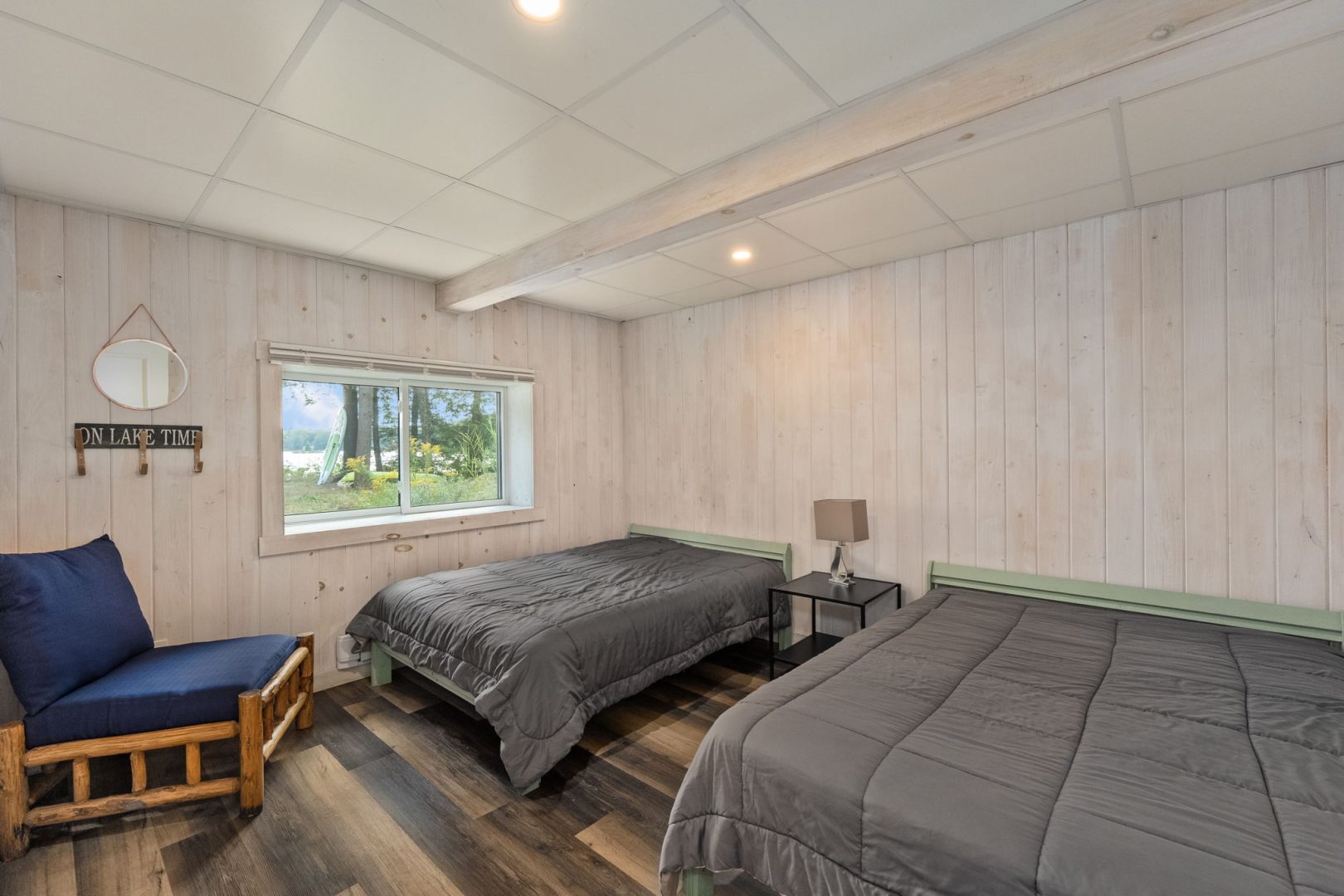 Two grey beds in a white bedroom with a large window