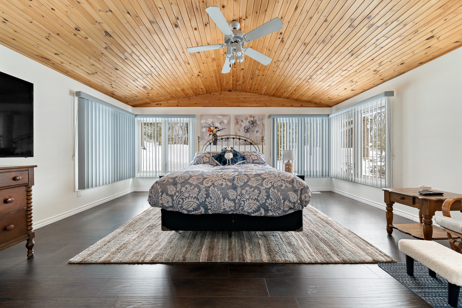 A patterned bed on a striped carpet in a spacious bedroom with windows